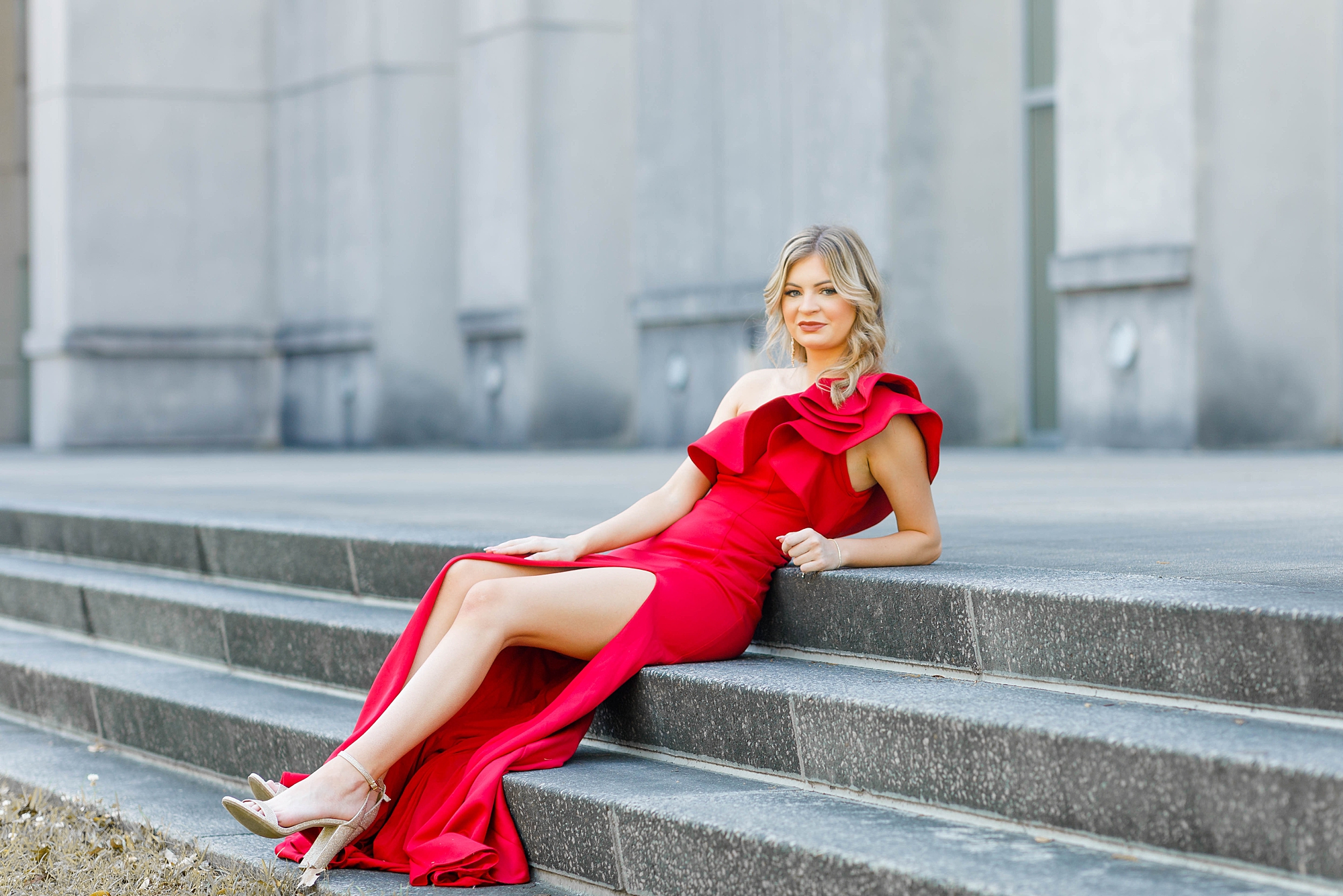 senior in elegant red dress sitting on steps of historic building in downtown Baton Rouge